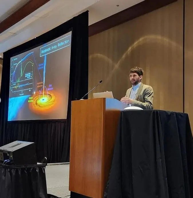Thomas Dauser giving an invited talk at an AAS meeting in April 2024 after having been awarded with the Innovation Prize Thomas Dauser giving an invited talk at an AAS meeting in April 2024 after having been awarded with the Innovation Prize. A man giving a talk is shown, next to him a big screen showing a slide from a slide show with a sketch about relativistic X-ray reflection.