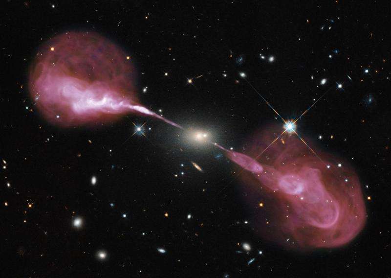 The FR II radio galaxy Hercules A (3C 348) as detected by the Karl G. Jansky Very Large Array in New Mexico is shown in pink/purple colours. Jets and radio lobes extend far beyond the host galaxy (image centre). A Hubble Space Telescope exposure showing the emission of the elliptical host galaxy in visible light as well as numbers of background galaxies and one foreground star (right of image centre) in the Milky Way Galaxy are overlaid. The FR II radio galaxy Hercules A (3C 348) as detected by the Karl G. Jansky Very Large Array in New Mexico is shown in pink/purple colours. Jets and radio lobes extend far beyond the host galaxy (image centre). A Hubble Space Telescope exposure showing the emission of the elliptical host galaxy in visible light as well as numbers of background galaxies and one foreground star (right of image centre) in our own Milky Way Galaxy are overlaid on the radio image.