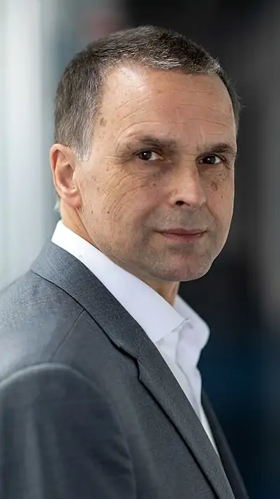 Profile picture of the awardee Anton Zensus. The upper body and the head of a man with grey-black, short hairs, dressed in a white shirt and dark-grey jacket is shown.