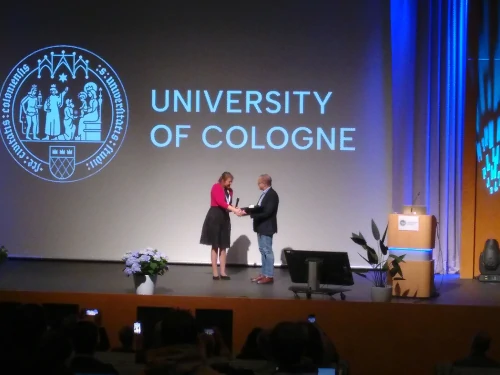 Prof. Zensus receives the Schwarzschild Medal by AG president Prof. Stefanie Walch-Gassner during the annual meeting of the AG. Both persons are standing on the podium in front of a large screen and are shaking hands. Image credit: Christoph Wendel