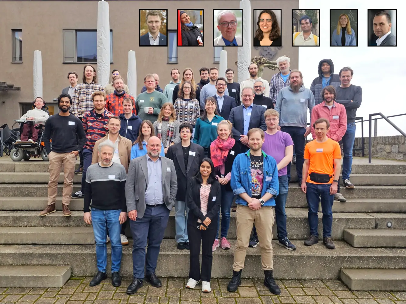 Group picture of the participants of the annual assembly 2025. A group picture of the participants of the annual assembly 2025. The picture shows about 35 persons standing in front of and on stairs. In the background a grey building is visible. At the top, seven inset pictures show the faces of the remote participants.